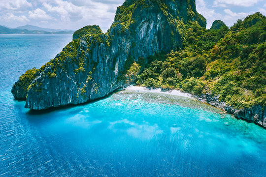 El Nido, Palawan. Aerial drone view of tropical Entalula Island. Huge steep rocks cliffs mountains with blue bay and beautiful intact coral reef. Island hopping tour trip