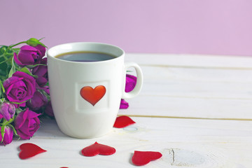 Valentine's Day breakfast. White tea mug with a heart pattern and  homemade cupcake with candles, hearts next to a bouquet of roses and a box with a gift on a wooden table. Copy space