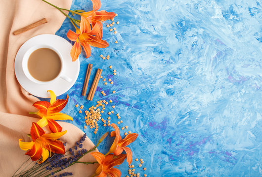 Orange Day-lily And Lavender Flowers And A Cup Of Coffee On A Blue Concrete Background, With Orange Textile. Top View.