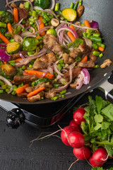Roasting meat with vegetables, on a black wooden background. Culinary, gastronomy. Vertical frame. Tasty and healthy food.