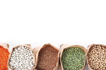 Fototapeta na wymiar Different types of legumes and cereals in paper bags on white background, top view. Organic grains