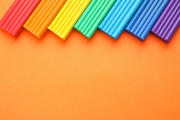 Colorful bars of modeling clay on orange background, flat lay with space for text. Rainbow palette