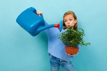 European girl with a watering can and a plant in her hands on a light blue background © Ivan Traimak