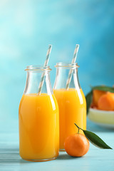 Bottles of fresh tangerine juice on blue wooden background