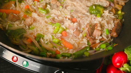 Frying and cooking rice and meat in a wok with vegetables, on a black wooden background, with space. Culinary background, gastronomy, Asian and Oriental cuisine. Thailand