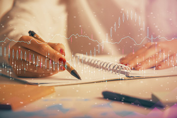 Double exposure of woman's hands making notes with forex graph hologram. Concept technical analysis.