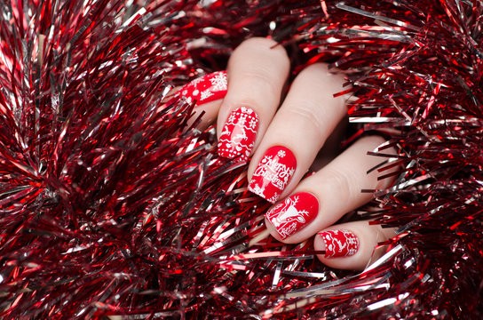 red Christmas manicure with deer and snowflakes and Norwegian pattern on the background of shiny tinsel
