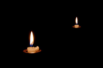 Two candles burning in the dark. The candles almost burned out.