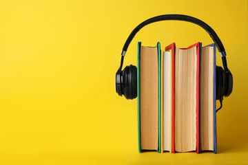 Books with modern headphones on yellow background. Space for text
