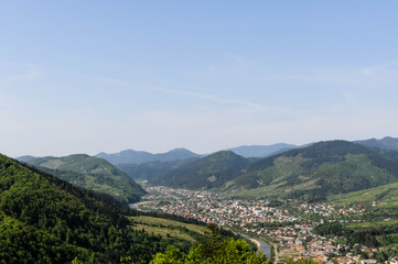 landscape of blue sky and town near big river in valley among mountains covered green forest