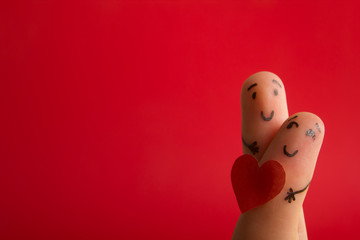 Valentines day fall in love concept. Painted happy funny fingers smiley holding red heart against red background with copy space for ad text