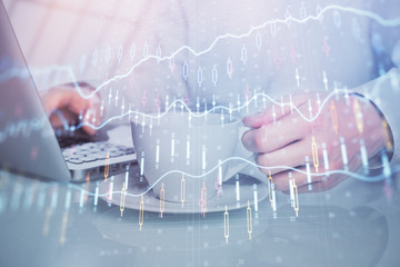 Double exposure of graph with man typing on computer in office on background. Concept of hard work.