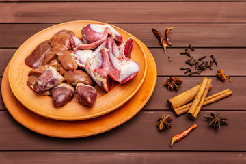 Fresh raw duck offal: heart, liver, stomach. Dry spices: cinnamon, star anise, clove, chili pepper. Wooden boards background