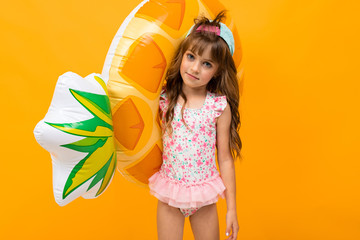 child with a baseball cap in a swimsuit with a swimming circle, pineapple on an orange background