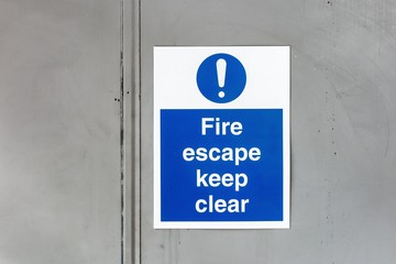 The sign Fire escape Keep clear on a grey metal door warning other not to stay in this hazardous...