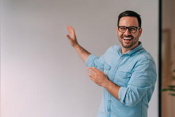 Portrait of happy young businessman pointing at white wall