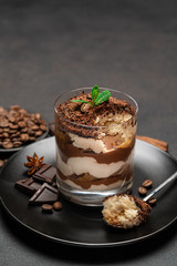 Classic tiramisu dessert in a glass cup and pieces of chocolate on dark concrete background