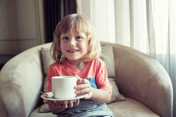 Portrait of smiling baby boy with cup on the chair