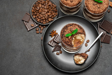 Classic tiramisu dessert in a glass cup and pieces of chocolate on dark concrete background