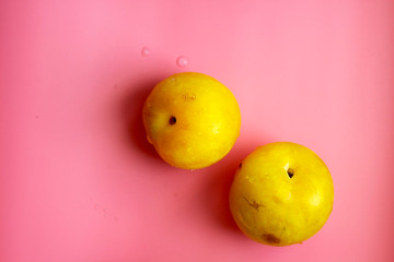 Flat lay composition with yellow plums and space for text on color pink background.