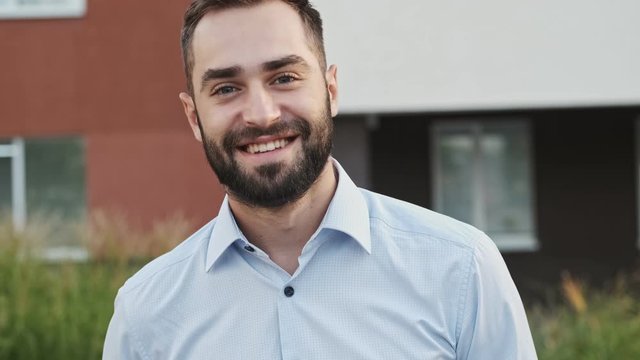 Cool happy bearded businessman looking at the camera and posing outdoors