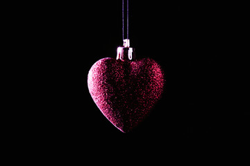 Red Christmas bauble over dark background. Low key photo. Heart shape.