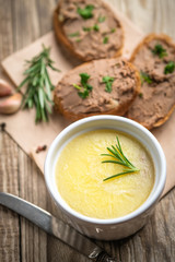 Fresh homemade chicken liver pate in ceramic bowl or ramekin and baguette slices with pate with herbs and garlic on a rustic wooden background. Top view.