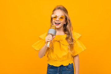 Nice little girl with her glasses sings songs into the microphone isolated on white background