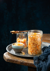 Homemade fermented cabbage kimchi sauerkraut, sour glass jars over rustic kitchen table, dark background, copy space. Fermented preserved vegetarian superfoods concept. Canned probiotic food .