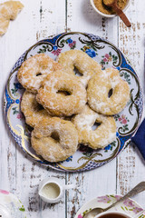 An up down view of a dish with ring-shaped pastries over a white wooden table