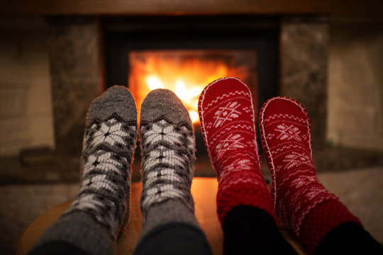 Legs in winter socks with a pattern on the background of a burning fireplace. Cozy winter atmosphere