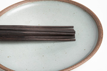 Six Pairs Of Sculptural Black Chopsticks On Stoneware Plate
