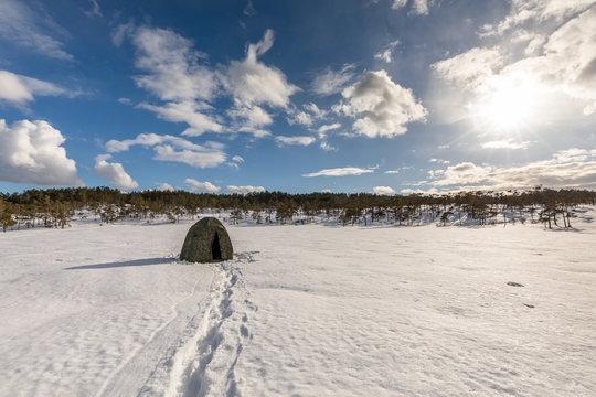 Camouflage tent on a snow covered bog with cloudy sky