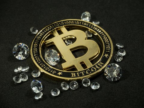 Shiny gold bitcoin virtual currency coin laying on black table with diamonds