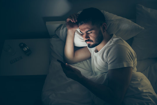 Top above high angle view portrait of his he nice attractive focused guy lying in bed using digital cell insomnia at night late evening home dark illuminated room flat house indoors