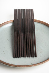 Six Pairs Of Sculptural Black Chopsticks On Stoneware Plate