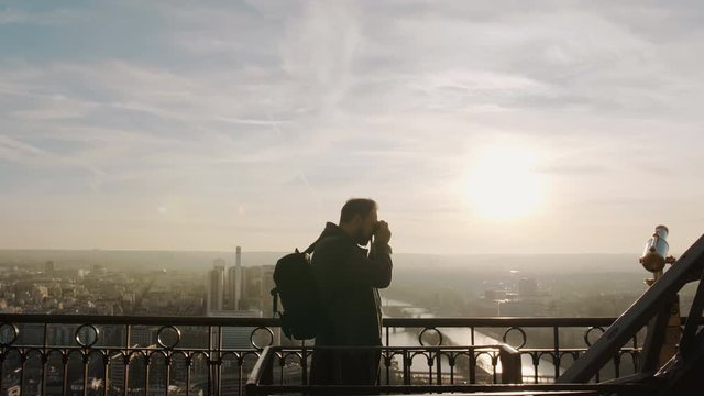 Young happy tourist man with camera and backpack taking photos of epic Paris sunset on top of Eiffel Tower slow motion.