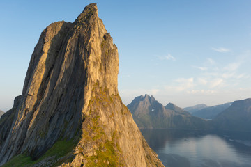 Cliff wall bathed in evening sun. The mountain top Segla shaped as a sail. In the background the Norwegian fjord Mefjord and mountains.