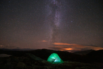 Milky way and starry sky over night scene outdoors in the forest and the mountains with green tent infront. Landscape, astronomy and camping concept.