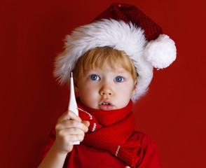 Little boy in a red santa hat holds a thermometer. The child is sick before Christmas