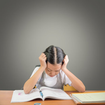 Stressed schoolgirl doing homework and preparing for exams. Young Asian student girl hard at work isolated with grey background and copy space. Education concept.