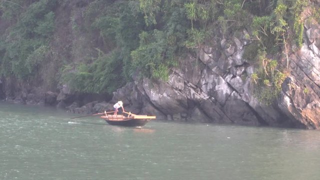 Man standing up, rowing small wooden boat in Halong Bay Vietnam