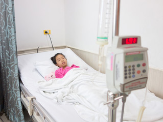 Ill young Asian girl sleeping on bed in hospital. Sick kid with Intravenous infusion.