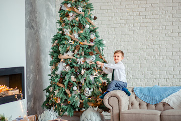 Cute boy decorates the Christmas tree with Christmas balls, gifts under the Christmas tree.