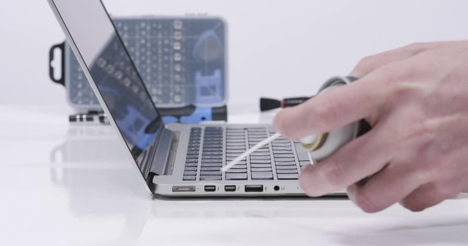 Service worker cleaning laptop connection plugs with compressed air in white walled lab in 4k