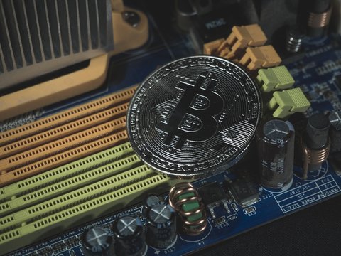 Shiny silver bitcoin virtual crypto currency coin laying on electronic circuit motherboard computer