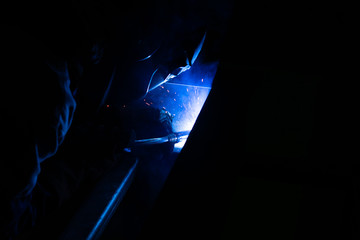 Masked welder works at the factory on metal welding. Sparks and smoke fly. Industrial photo.