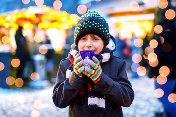 Little cute kid boy drinking hot children punch or chocolate on German Christmas market. Happy...