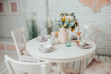 White dining room interior design. White round table with flowers, candles and cups.