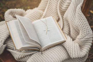 The Bible and the cross lie on a warm sweater. Concept for faith, spirituality and religion.